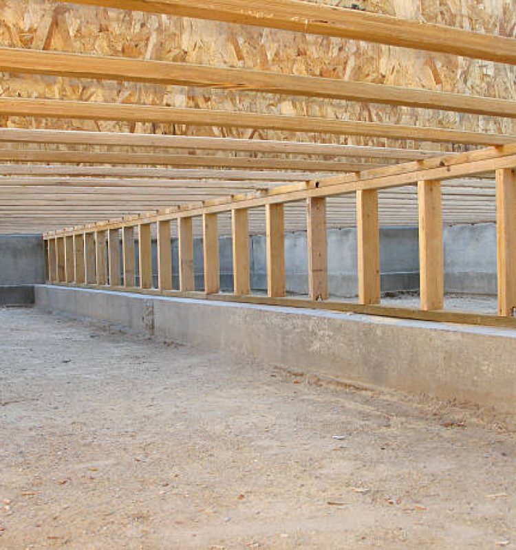 This color photo shows a view of the crawlspace foundation beneath the framing of a new house under construction. Floor joists and a pony wall (short support wall) on a concrete footer are clearly visible. The crawlspace floor is neat and clean. The image is in landscape orientation.
